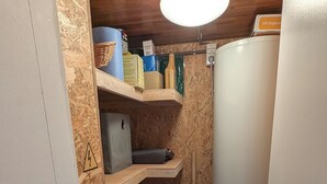 Een kleine bijkeuken met houten planken, een boiler en diverse opbergmanden.