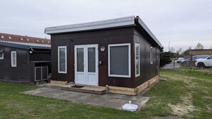 Een klein, donker houten gebouw met een witte deur en ramen, een klein terras, en een bord met het nummer 11 aan de muur.