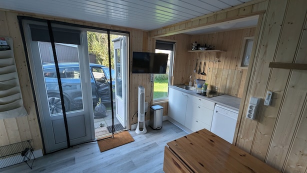 Een compacte keuken met een schuifdeur van glas naar een auto, een klein spoelgedeelte en een televisie bevestigd boven het aanrecht.