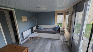 Een knus vertrek met een inbouwkbankbed, een klein tafeltje en een raam met uitzicht op een bakstenen muur en groen buiten.
