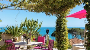 Eine Terrasse mit Tisch und Stühlen, eine Kamera auf einem Stativ und Blick aufs Meer.