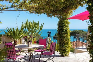 Eine Terrasse mit Tisch und Stühlen, eine Kamera auf einem Stativ und Blick aufs Meer.