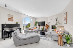 Ein modernes Wohnzimmer mit Klavier, Sofas, Fernseher und einem großen Fenster.