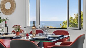 Ein Esszimmer mit Tisch für vier Personen, großen Fenstern mit Meerblick und einem dekorativen Wandbild.