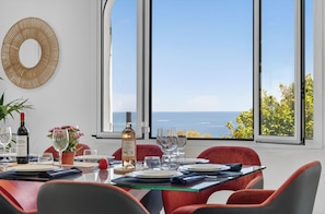 Ein Esszimmer mit Tisch für vier Personen, großen Fenstern mit Meerblick und einem dekorativen Wandbild.