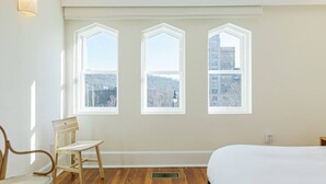 A room with three large windows, a wooden chair, a bed, and a wall-mounted light fixture. - The Gazette Condo 200 at ATB (Asheville)