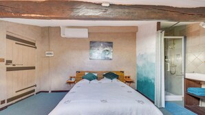 A bedroom with a large bed, a wooden headboard, a painting on the wall, a bathroom with a shower, and a wooden wardrobe. - Villa Pauill'art - Marco Polo  (Pauillac)