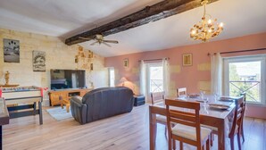 A cozy living room with a wooden ceiling, a sofa, a dining table set for four, and a television. - Villa Pauill'art - Marco Polo  (Pauillac)