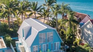 A blue house with a balcony, surrounded by palm trees and a view of the ocean. - Ocean Front Paradise @ Sea Beach (Aguada)
