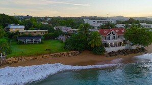 A coastal property with a beach, a large house with a red roof, and surrounding greenery. - Ocean Front Paradise @ Sea Beach (Aguada)