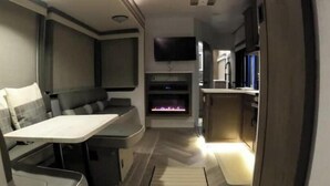 A compact RV interior with a kitchenette, seating area, and a flat-screen TV mounted on the wall. - Ocean Front Paradise @ Sea Beach (Aguada)