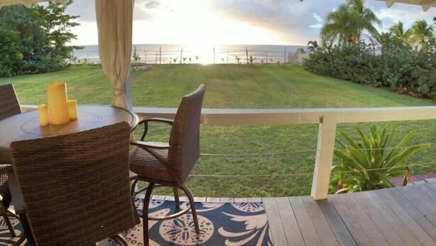 A covered outdoor seating area with a table and chairs, overlooking a grassy lawn and a view of the ocean. - Ocean Front Paradise @ Sea Beach (Aguada)