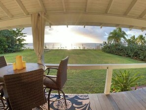 A covered outdoor seating area with a table and chairs, overlooking a grassy lawn and a view of the ocean. - Ocean Front Paradise @ Sea Beach (Aguada)