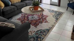 Un soggiorno con divano, tavolino, una pianta in vaso e un tappeto decorato.