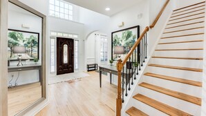 Une pièce spacieuse dotée de planchers en bois, d’un grand miroir, d’un escalier en bois et d’une porte avec un panneau de verre.
