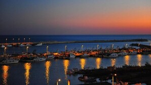 Un port de plaisance au crépuscule, avec des bateaux amarrés et des lumières se reflétant sur l’eau.