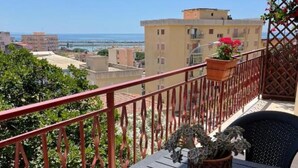 Un balcon avec une table et des chaises, un pot de fleurs et une vue sur la mer et les bâtiments.
