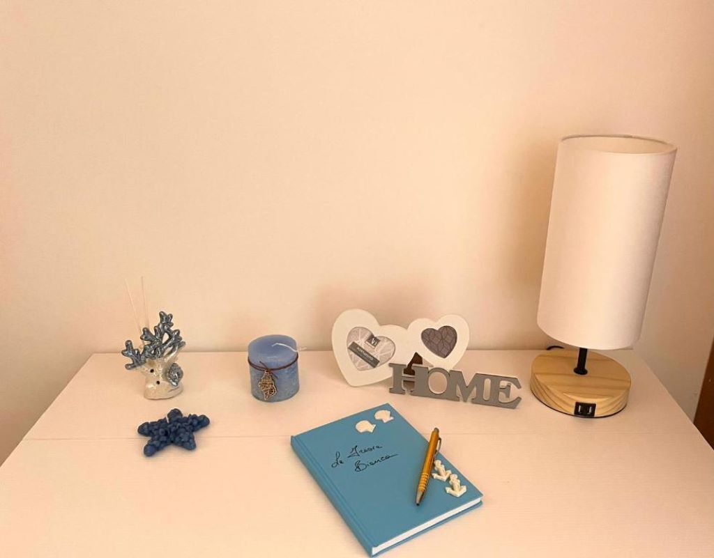 A bedside table with a lamp, a notebook, decorative items, and a sign that reads "HOME".