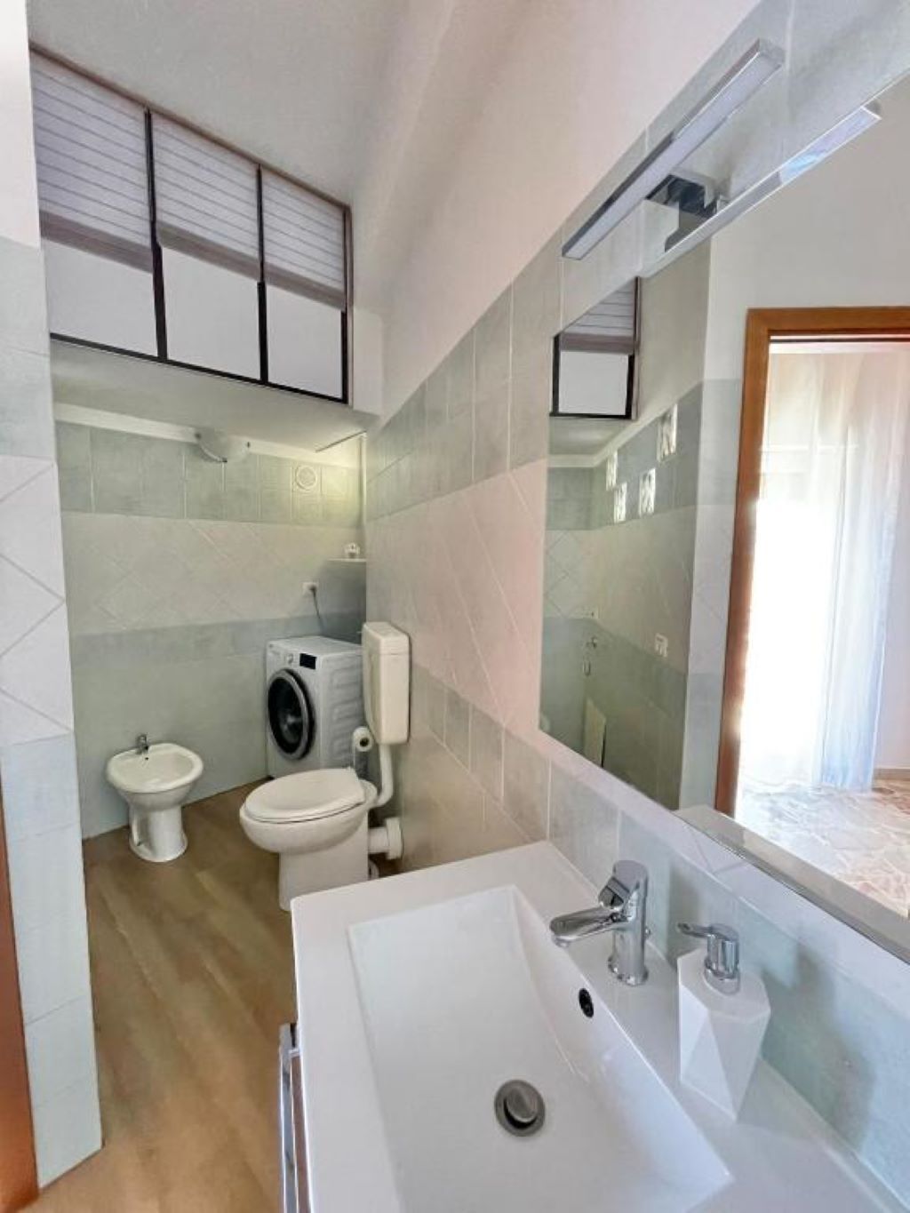 Ein modernes Badezimmer mit einem weißen Waschbecken, einem Bidet, einer Toilette und einer Waschmaschine.