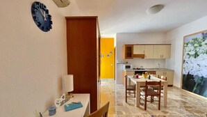 Un espace de vie compact comprenant un coin repas, une cuisine et une grande fenêtre donnant sur un jardin fleuri.