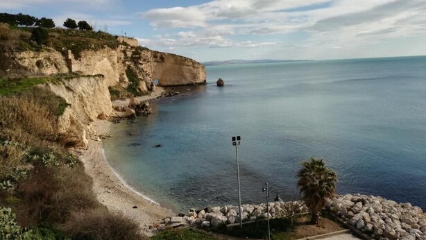 Un paysage côtier offrant une vue dégagée sur la mer, une plage de sable et des falaises rocheuses.