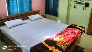 A room with a bed, a TV mounted on the wall, and a window with curtains. - Sadhu Inn (Puri)