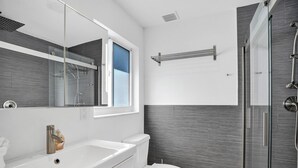A modern bathroom with a white sink, a toilet, and a shower area.