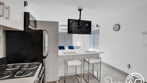 A modern kitchen with a stove, refrigerator, and bar stools.