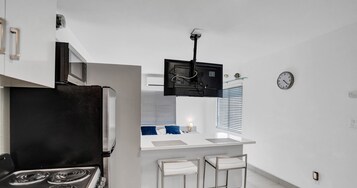 Cocina compacta con estufa, microondas y pequeño comedor con dos taburetes de bar.