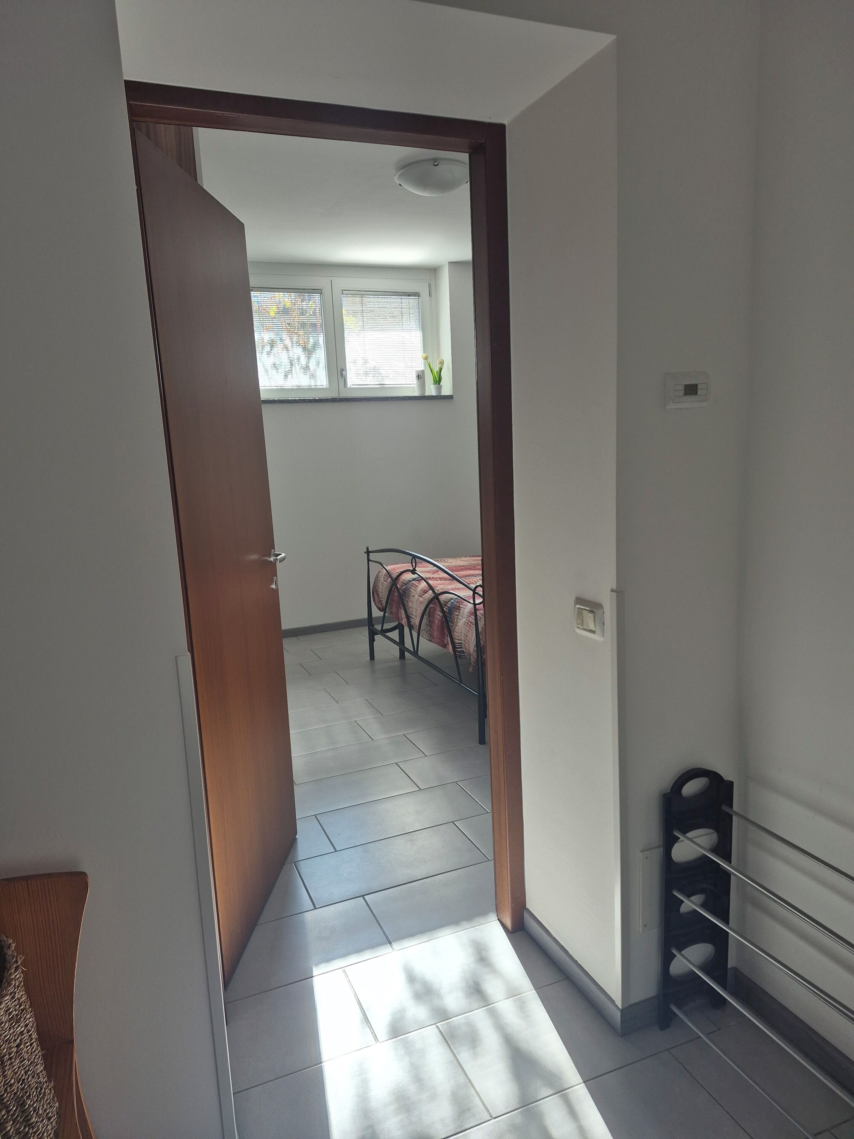 Een gang die leidt naar een slaapkamer met een bed, een raam en een radiator.