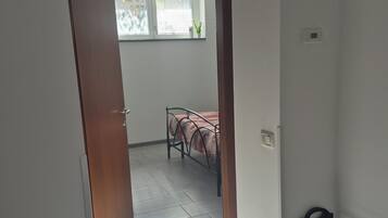 Een gang die leidt naar een slaapkamer met een bed, een raam en een radiator.