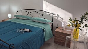 Ein Schlafzimmer mit Bett, Nachttisch, einer Nachttischlampe, einer Wand-Klimaanlage, einem Fenster mit Jalousien und einem Bild an der Wand.