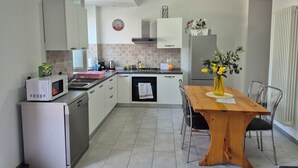 Eine kleine Küche mit weißen Schränken, einer Mikrowelle, einem Kühlschrank und einem Esstisch mit Stühlen.