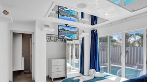 Quarto de hotel moderno com varanda, piscina e duas televisões na parede.
