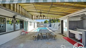 Uma área externa coberta com piscina, mesa de piquenique e cozinha.