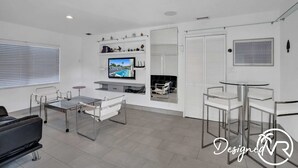 Una sala de estar moderna con un televisor de pantalla plana, un sofá, una mesa de centro y un comedor con sillas y una mesa de vidrio.