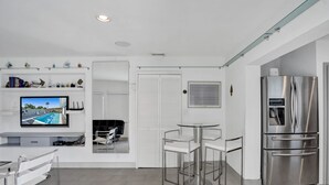 Uma cozinha moderna com geladeira de aço inoxidável, TV de tela plana na parede e área de jantar com mesa de vidro e cadeiras de metal.