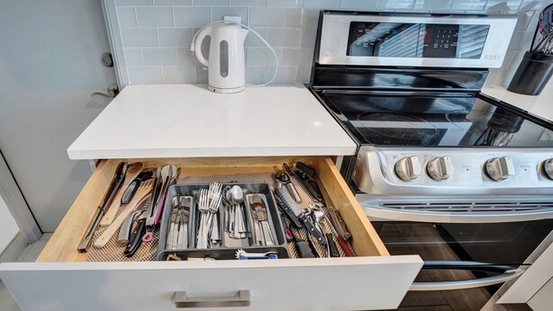 Una cocina con un cajón que contiene varios utensilios, un hervidor y una estufa.