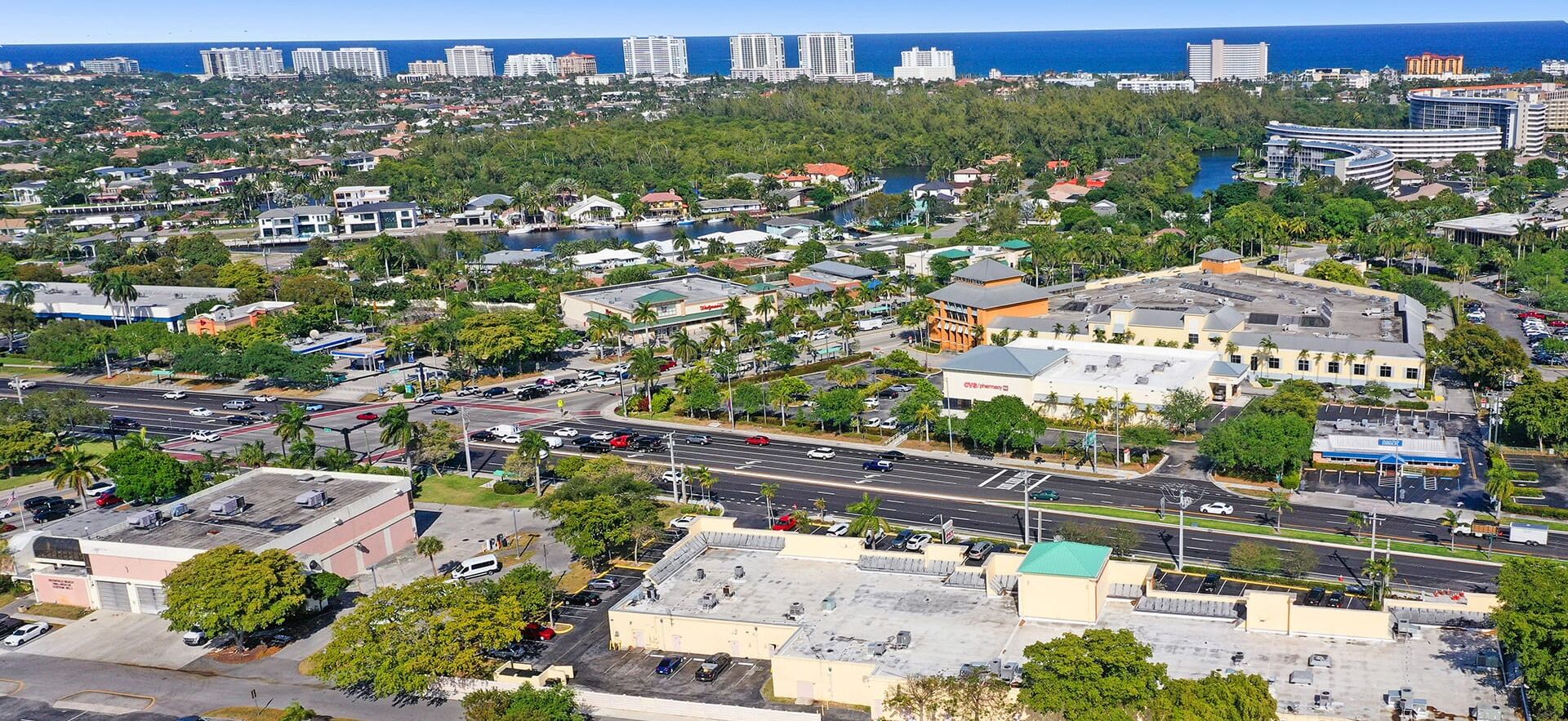 An aerial view of a coastal city with a mix of residential and commercial buildings, a prominent CVS Pharmacy, and a marina with boats.