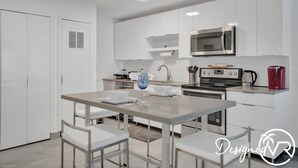 Une cuisine moderne avec des meubles blancs, un four à micro-ondes, une machine à café et une table à manger avec des chaises.