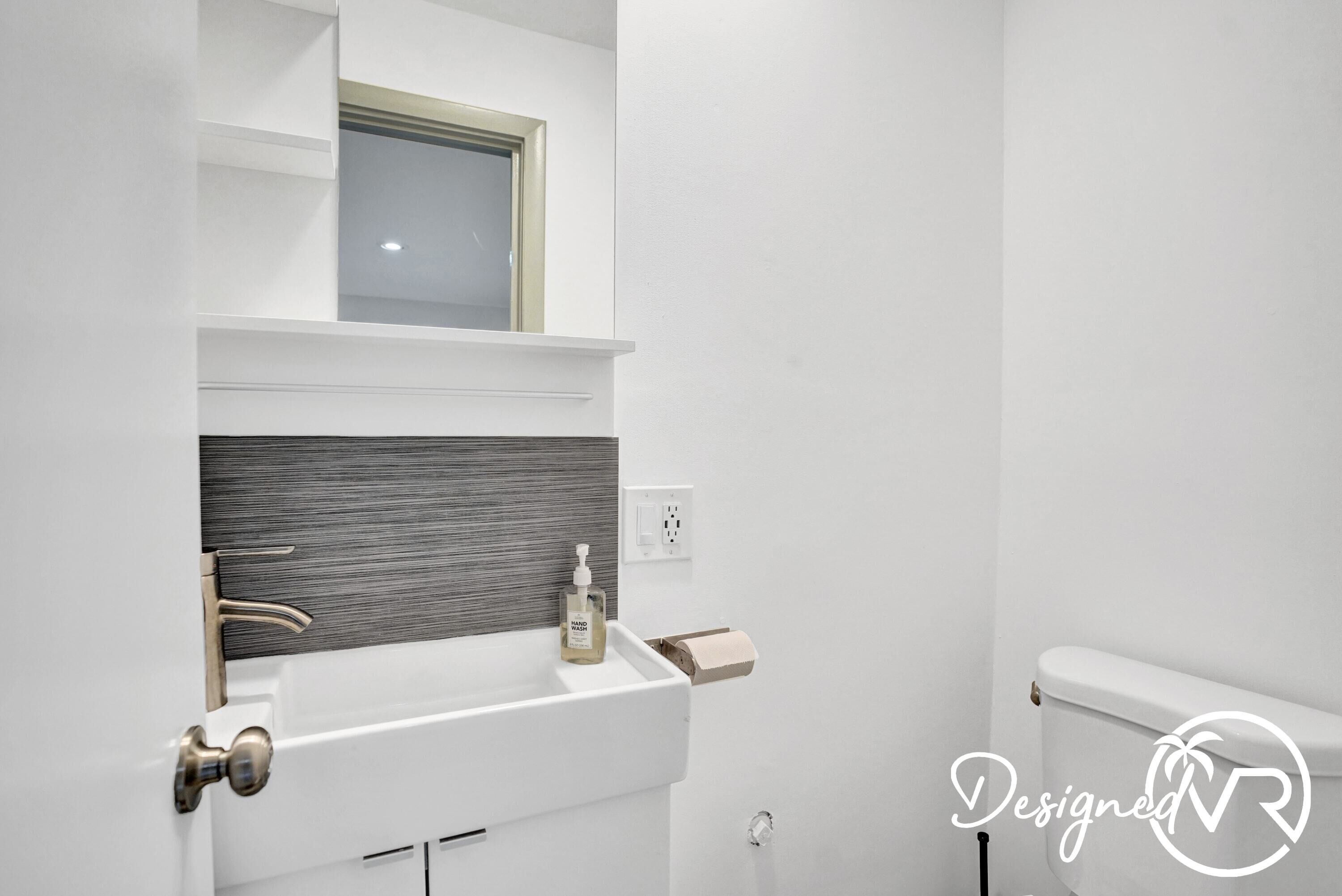 Une salle de bain avec un lavabo blanc, une fenêtre au-dessus du miroir et des toilettes.