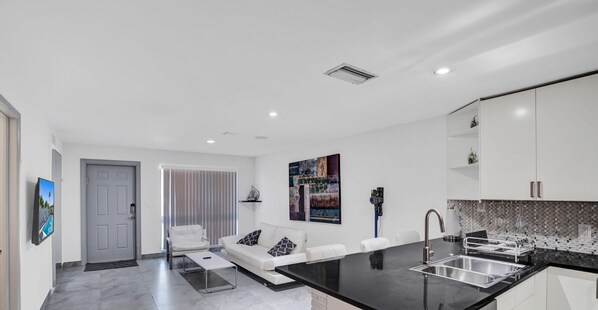 A modern kitchen with a black countertop, white cabinets, and a stainless steel sink. - Unit E Sea&i Private House Near Deerfield Beach (Deerfield Beach)