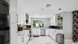 Una cocina moderna con armarios blancos, una campana de acero inoxidable, lavavajillas y un cubo de basura.
