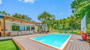 Una piscina con cubierta de madera, un área de estar techada y vistas a un paisaje verde exuberante.