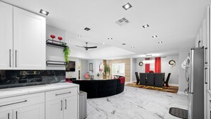 Una cocina moderna con armarios blancos, una isla negra y suelo de mármol.