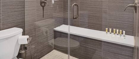 Een moderne badkamer met een douchecabine van glas, een wit toilet en een wastafel met toiletartikelen.