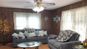 A living room with a grey sofa, a smaller grey armchair, a round coffee table, and a ceiling fan.