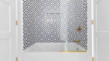 A bathroom with a geometric patterned wall, a clear shower enclosure, and gold fixtures.