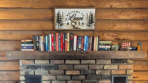 Una chimenea con repisa de madera que muestra libros, una señal encima y leña ardiendo en su interior.
