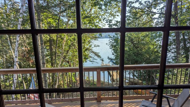 Terraza con dos sillas y una mesa, con vista a un lago rodeado de árboles.